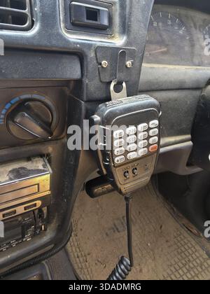 Primo piano del microfono per radio ricetrasmittenti vintage con tastiera montata sul supporto all'interno di un'auto polverosa. Questa vecchia apparecchiatura di comunicazione sul cruscotto evoca funzioni Foto Stock