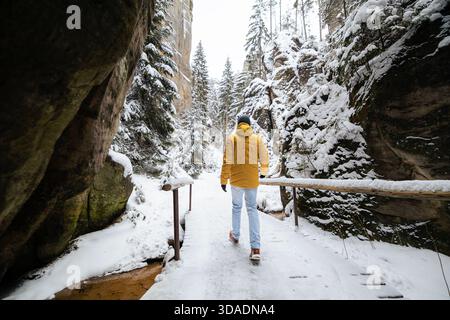 Uomo in abiti caldi che cammina attraverso il paesaggio innevato tra alte formazioni rocciose ad Adrspach in un freddo giorno d'inverno. La scena cattura i momenti più tranquilli all'aperto Foto Stock