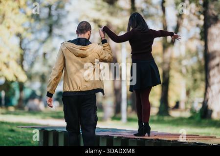 Coppia che si gode un momento di gioco nel parco, braccia sollevate, bilanciate su una piattaforma di legno sotto la luce del sole Foto Stock