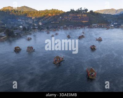Serena vista aerea del villaggio galleggiante di una casa di zattera sul lago nebbioso all'alba. Tranquillo paesaggio montano in Thailandia che offre pace e bellezza Foto Stock
