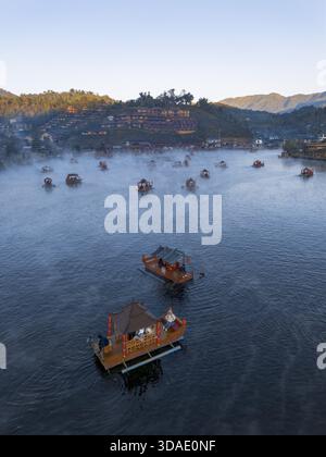 Tranquillo paesaggio mattutino di un villaggio tradizionale in Thailandia. la barca in legno per viaggi e turismo galleggia sul lago calmo, circondato da una tranquilla cresta nebulizzata Foto Stock