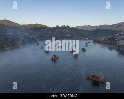 La tranquilla vista aerea mostra il villaggio galleggiante sul tranquillo lago durante la splendida alba. acque calme e tranquillo paesaggio montano con nebbia mattutina crea Foto Stock