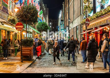 Affollato viale Temple Bar di notte, decorato con bandiere, luci festive e vivaci pedoni su ciottoli. Foto Stock