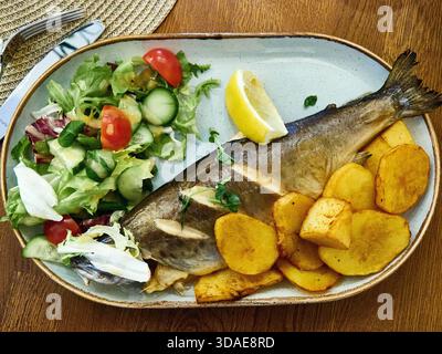 Trota arrosto servita con patate dorate e insalata fresca Foto Stock