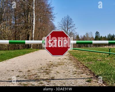 Segnale DI STOP rosso su una barriera verde e bianca che blocca una strada rurale Foto Stock