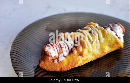 Una vista sul delizioso panino con salsicce salate. La pasticceria al forno dorata è ripiena di salsiccia di carne e condita con maionese, ketchup, e. Foto Stock