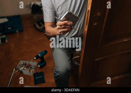 Dettaglio immagine ritagliata di un tuttofare che installa il meccanismo di blocco della porta nel telaio della porta, eseguendo interventi di riparazione e manutenzione essenziali, migliorando la sicurezza domestica Foto Stock