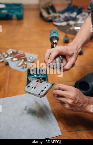 Getto verticale del meccanismo di lubrificazione maschio della serratura della porta del falegname con olio spray, che esegue interventi di manutenzione domestica o di riparazione fai da te per evitare l'inceppamento e. Foto Stock