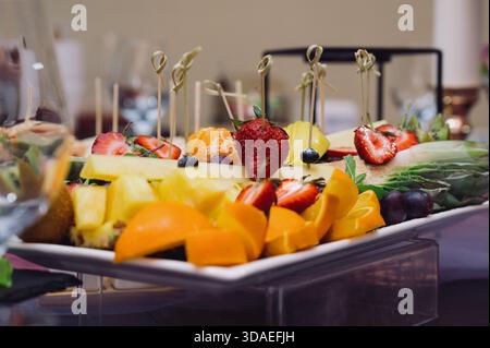 Un ricco assortimento di frutta fresca a fette: Fragole, ananas, arancia e mandarino su un tavolo festivo. Primo piano di un piatto da portata con un piatto fresco Foto Stock