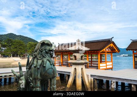 Passerelle in legno del Santuario di Itsukushima e statua del cane da leone komainu. Giappone Foto Stock