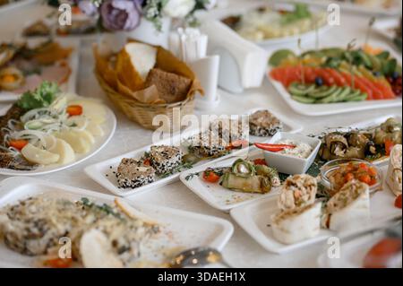 Una varietà di antipasti freddi e insalate sono servite sul tavolo del banchetto. Abbondanza di antipasti in porzioni di carne, pesce e verdure su bianco PL Foto Stock