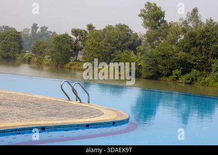 La piscina a sfioro del resort di lusso presenta un bordo curvo e una terrazza piastrellata, offrendo una vista panoramica del corpo naturale dell'acqua e dei dintorni Foto Stock