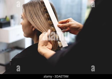 Parrucchiere che controlla il colore dei capelli della donna con una tabella di ombreggiatura professionale nel moderno salone di bellezza, valutando con precisione le tonalità e le evidenziazioni durante Foto Stock