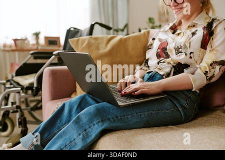 Giovane donna adulta che digita sul notebook mentre si rilassa con disabilità Foto Stock