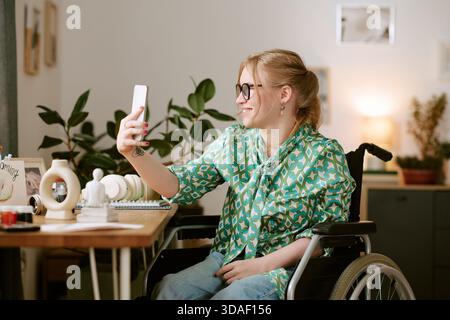 Giovane donna con disabilità sorride mentre porta Selfie in casa Foto Stock