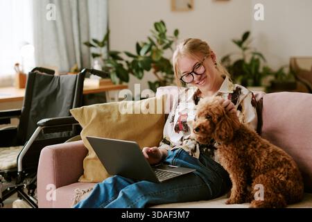 Giovane donna adulta con disabilità che utilizza un laptop e un cane da compagnia Foto Stock