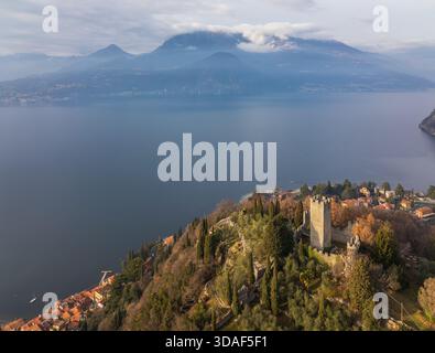 Veduta aerea del Castello di Vezio in piedi a guardia delle tranquille acque, una fortezza contro i secoli, con montagne ricoperte di nebbia, Varenna, Lombar Foto Stock