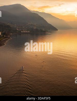 Vista aerea della luce dorata che bagna le acque tranquille vicino alle rive montuose, proiettando un caldo bagliore su Varenna, Lombardia, Italia. Foto Stock