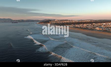 Vista aerea delle onde che si infrangono sulla spiaggia sabbiosa, un vibrante contrasto con il paesaggio urbano sotto un cielo morbido e pastello, San Francisco, California, Unit Foto Stock