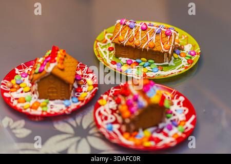 Vista ravvicinata di tre colorate case di pan di zenzero decorate con glassa e caramelle su luminosi piatti natalizi. Svezia. Foto Stock