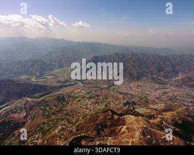 Veduta aerea della vasta città annidata tra aspre montagne ocra e un fiume tortuoso, sotto un vasto cielo, Muzaffarabad, Azad Kashmir, Pakistan. Foto Stock