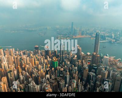 Veduta aerea dei grattacieli che penetrano nella nebbia, rivelando un vivace skyline con l'iconica Bank of China Tower e Victoria Harbour, Hong Kong, Foto Stock