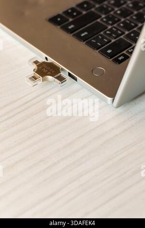 Foto dettagliata dell'area della tastiera di un laptop color argento con un'unità USB multi-porta in tonalità oro collegata, su uno sfondo di legno chiaro, che enfatizza la portabilità Foto Stock
