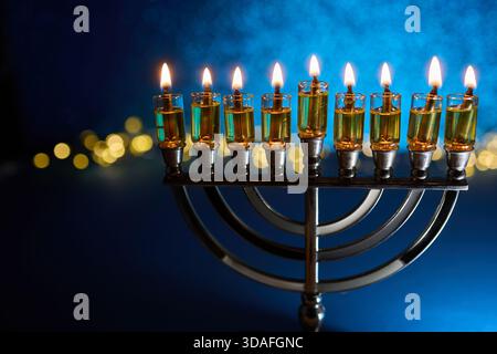 Hanukkah Menorah con candele accese. Menorah illuminata su sfondo blu scuro con luci bokeh Foto Stock