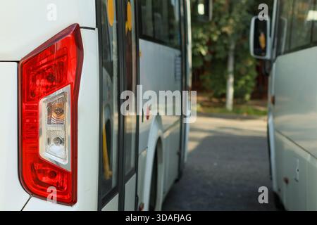 Dettaglio orizzontale del fanalino di coda rosso sull'autobus bianco in mezzo alla flotta parcheggiata vicino al verde durante la giornata intensa Foto Stock