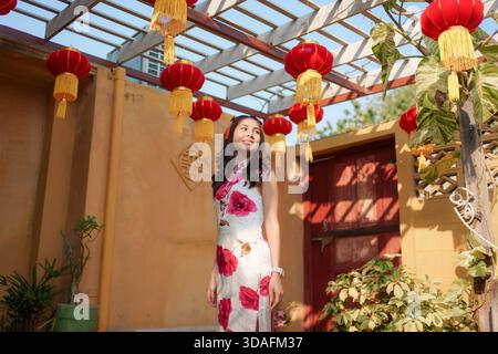 Felice donna asiatica in abito floreale o Cheongsam con lanterne rosse tradizionali nel tempio cinese durante il Capodanno cinese Foto Stock
