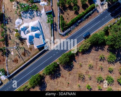 Vista aerea di un'auto solitaria scivola lungo una strada soleggiata che divide campi rustici e tradizionali abitazioni bianche, Monopoli, Puglia, Italia. Foto Stock