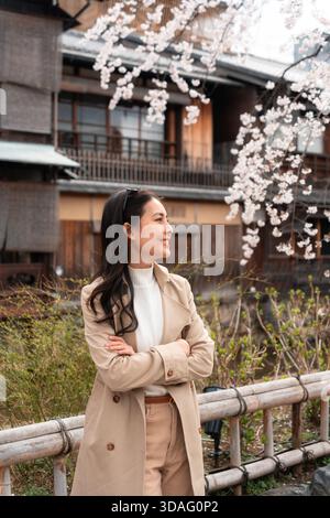 Ritratto di donna asiatica sorridente con la fioritura dei ciliegi vicino alla tradizionale casa giapponese in legno a Kyoto, Giappone Foto Stock
