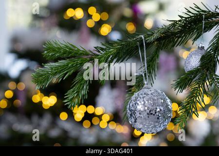 Baule natalizie in glitter argentato appeso a un ramo di pino con calde luci bokeh dorate sullo sfondo, eleganti decorazioni natalizie Foto Stock