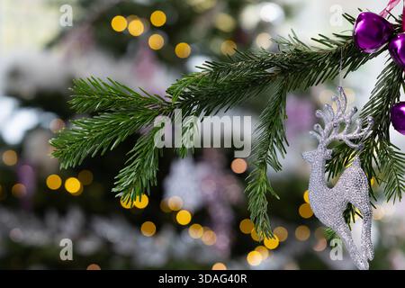 Ornamento in argento glitter Stag appeso a un ramo di pino con calde luci bokeh dorate sullo sfondo, eleganti decorazioni natalizie Foto Stock