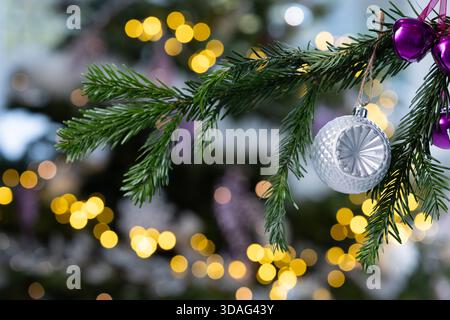 Baule natalizie in glitter argentato appeso a un ramo di pino con calde luci bokeh dorate sullo sfondo, eleganti decorazioni natalizie Foto Stock