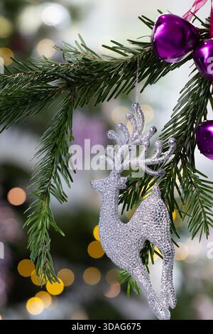 Ornamento in argento glitter Stag appeso a un ramo di pino con calde luci bokeh dorate sullo sfondo, eleganti decorazioni natalizie Foto Stock