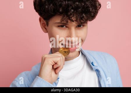 Giovane uomo con bitcoin su sfondo rosa che mostra interesse per il trading di criptovalute gli investimenti la finanza digitale e il denaro moderno Foto Stock