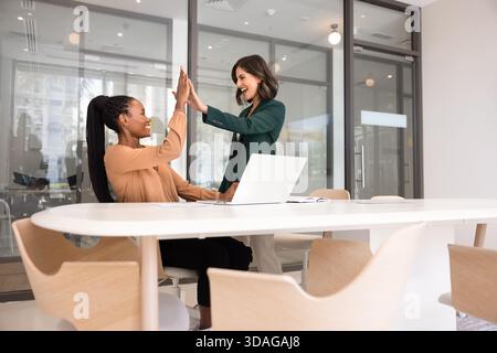 Due colleghe di sesso femminile eccitate, gioiose e diversificate, che celebrano il successo del lavoro di squadra Foto Stock