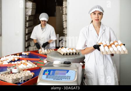 Giovane agricoltore europeo in uniforme che detiene una scatola di cartone piena di uova di pollo fresche dopo la cernita e l'etichettatura nell'azienda avicola Foto Stock