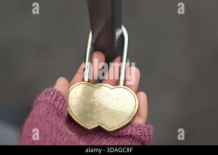 Donna che tiene a mano un lucchetto a forma di cuore su una ringhiera Foto Stock