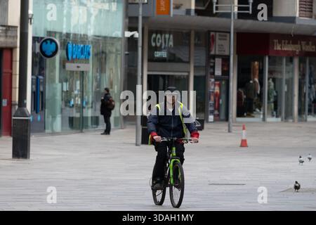 Un ciclista guida una bicicletta verde brillante lungo un'ampia strada asfaltata in un ambiente urbano. Il ciclista, un uomo che sembra avere 30 anni, indossa un jack scuro Foto Stock