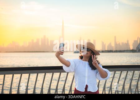 Giovane donna che scatta foto con il Burj Khalifa e lo skyline di Dubai al tramonto Foto Stock