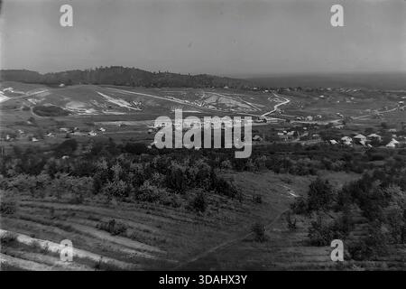 Bohorodychne, regione di Donetsk, RSS Ucraina, anni 1970 Una spettacolare vista panoramica archivistica ad alto angolo di una strada rurale di nuova costruzione con case in mattoni identiche annidate in una valle circondata da ondulate colline di gesso. Il paesaggio presenta giovani frutteti terrazzati sul pendio in primo piano e le caratteristiche scogliere bianche del rilievo Donbas in lontananza. Questo ampio scatto cattura l'espansione delle infrastrutture dei villaggi sovietici e la sua integrazione nell'ambiente naturale panoramico della pacifica regione. Foto Stock
