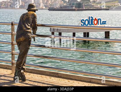 Baku, Azerbaigian - 10 maggio 2024: Statua in bronzo del pescatore sul viale Baku, con il Mar Caspio e lo skyline della città Foto Stock
