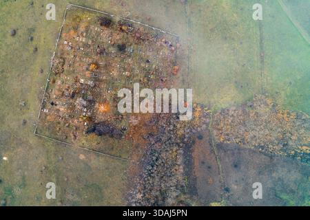 Vista dall'alto verso il basso di un cimitero rurale che mostra file ordinate di tombe e croci. Il sito solenne si trova in un paesaggio arido e ruvido vicino a una zona di conflitto militare attiva. Punto di vista dei droni. Foto Stock