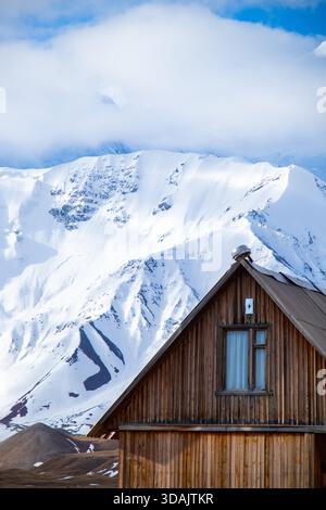 Primo piano del tetto di una cabina in legno e della finestra sullo sfondo di una massiccia vetta verticale ricoperta di neve Foto Stock