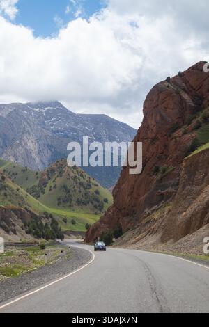 Regione di Naryn, Kirghizistan - 13 maggio 2024: Guida in auto su tortuose autostrade di montagna circondate da scogliere rosse e picchi aspri durante il giorno Foto Stock