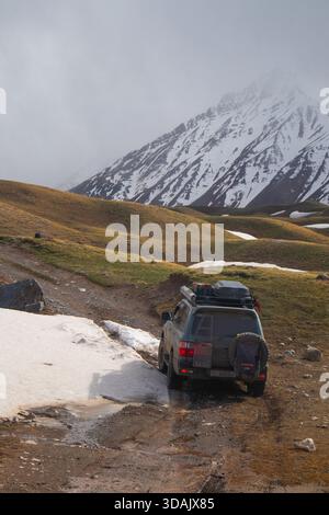 Regione di Naryn, Kirghizistan - 13 maggio 2024: SUV grigio che naviga su strade sterrate fangose con macchie di neve su terreni montani ad alta quota Foto Stock