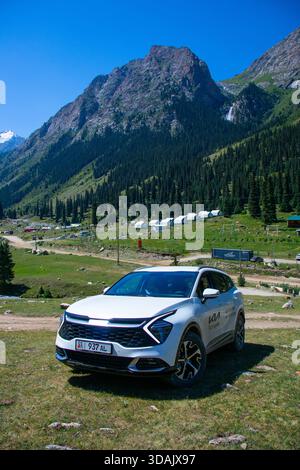 Regione di Naryn, Kirghizistan - 13 maggio 2024: SUV White Kia Sportage parcheggiato sull'erba con yurts tradizionali e montagne boscose sullo sfondo Foto Stock