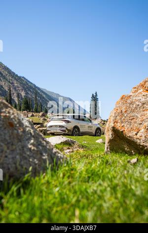 Regione di Naryn, Kirghizistan - 13 maggio 2024: SUV White Kia Sportage parcheggiato su un prato verde circondato da grandi rocce e montagne nella regione di Naryn Foto Stock